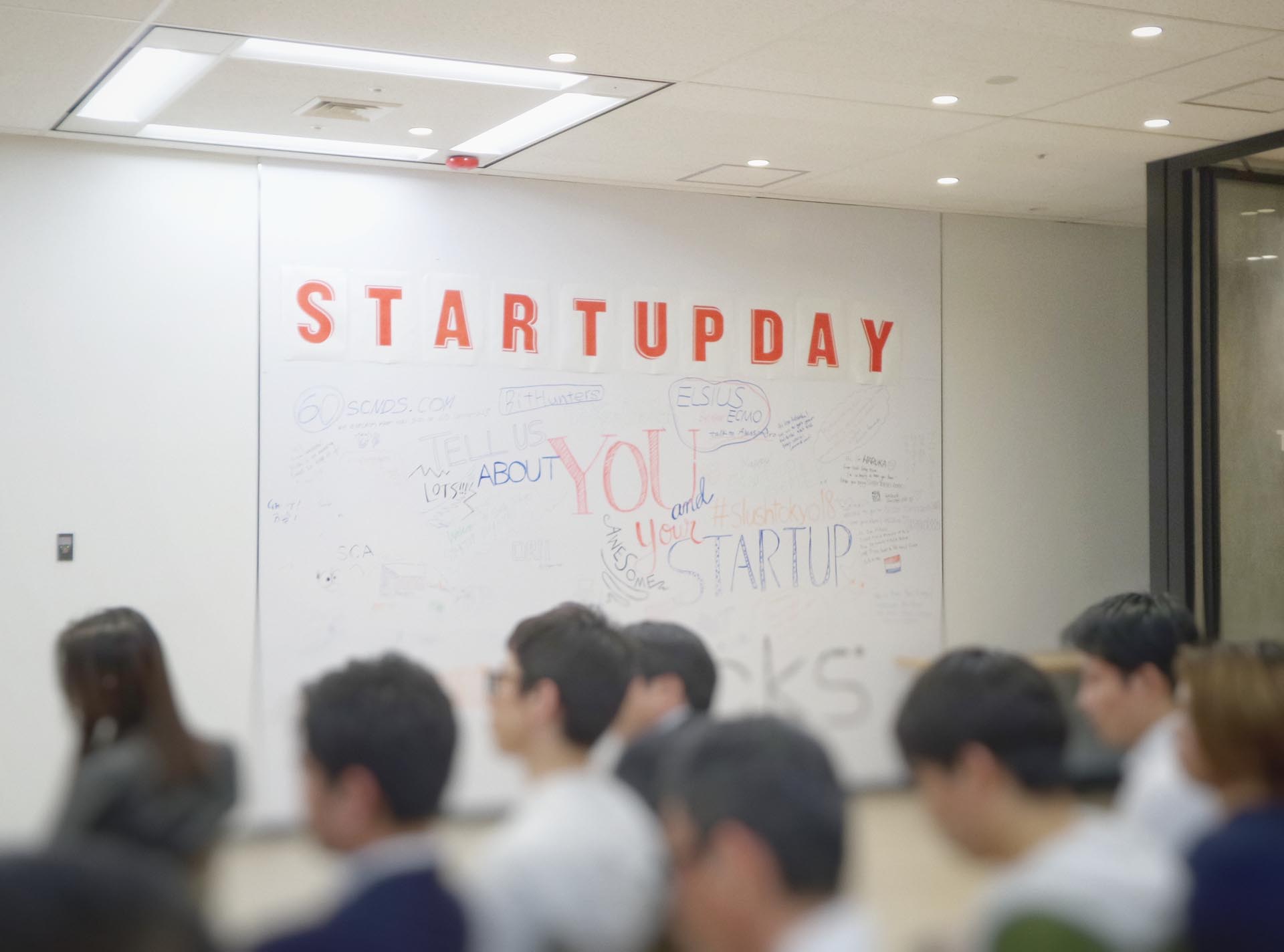 A space full of people in the foreground with focus on a whiteboard that says Startupday