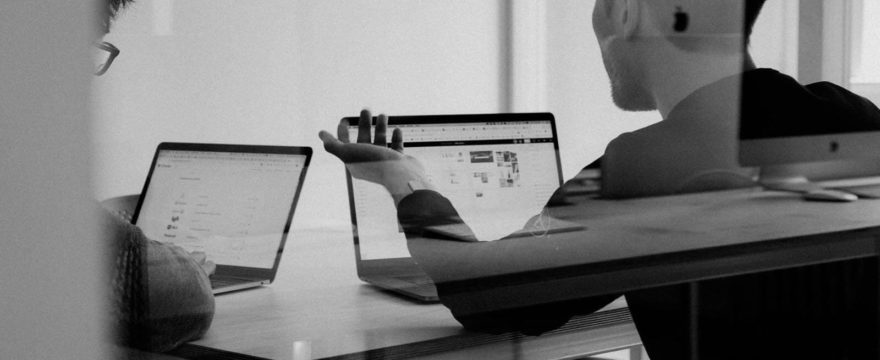 A black and white image of two people working together on laptops