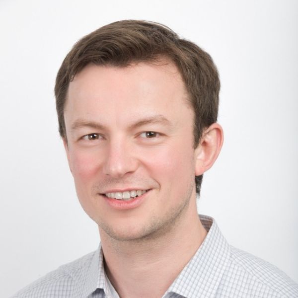 A man in a blue and white checked shirt smiles at the camera