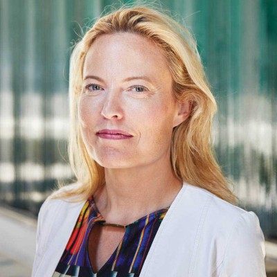 Woman with long blond hair and a white suit jacket looks at the camera