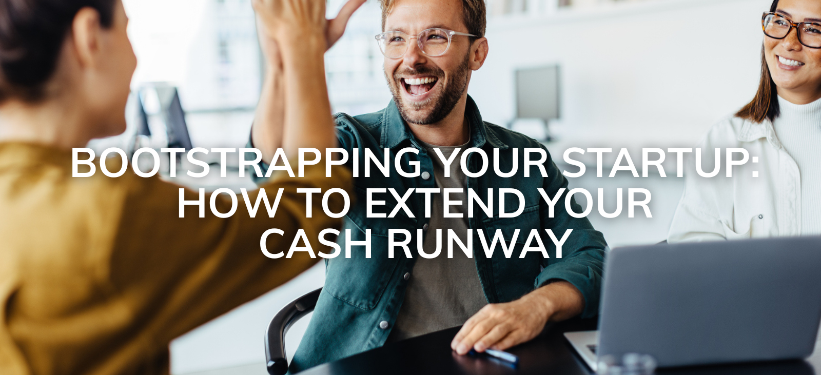 A man high fives his colleagues, with text overlay Bootstrapping your startup: How to extend your cash runway